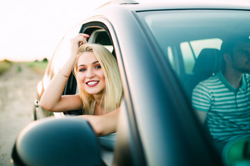Portrait of happy young woman going on a road trip leaning out of window. Female enjoying travelling in a car with her boyfriend.