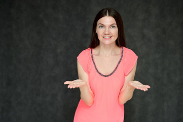 Portrait of a pretty young brunette woman with combed hair on a gray background in a pink blouse. It is in different poses. Looks straight at the camera. Slim figure.