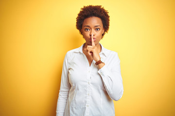 African american business woman over isolated yellow background asking to be quiet with finger on lips. Silence and secret concept.