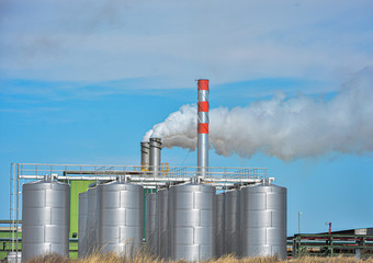 landscape of oil factory, metal drums and chimney with smoke on blue sky background