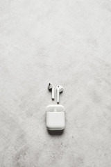 White wireless earphones or headphones and plastic case or box for storage and charging on grey concrete background. Top view. Copy space for text.