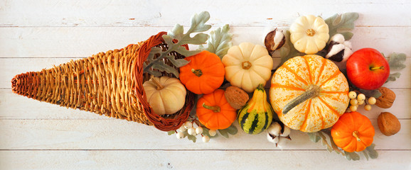 Thanksgiving cornucopia filled with autumn pumpkins and vegetables. Top view against a white wood...
