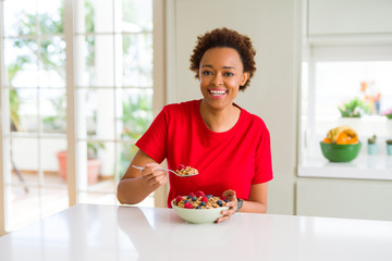Young beautiful african american woman with afro hair eating healthy wholemeal cereals and berries...