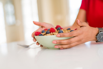 Close up of young woman eating healthy cereals and berries for breakfast