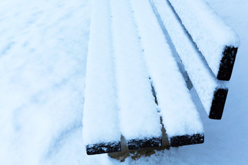 Side view of the wooden bench covered with a large layer of snow