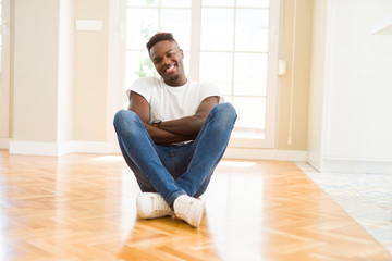 Handsome african american man sitting on the floor at home happy face smiling with crossed arms looking at the camera. Positive person.