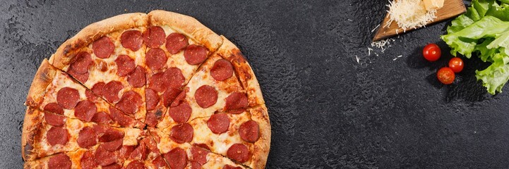 Pepperoni pizza on a black texture background. Still life. Top view.