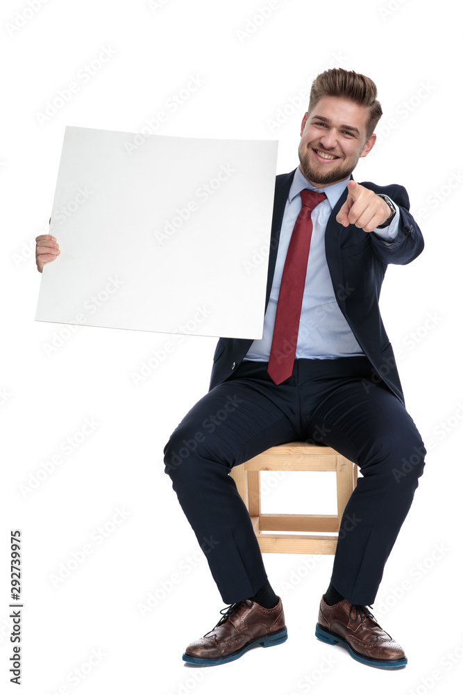 Poster happy young businessman holding empty board and pointing finger