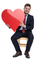 happy young businessman holding red heart in studio
