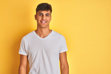 Fototapeta premium Young indian man wearing white t-shirt standing over isolated yellow background with a happy and cool smile on face. Lucky person.