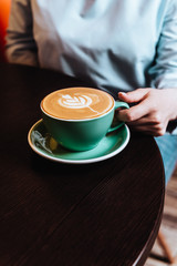 Female hands holding cyan cup of coffee cappuccino.