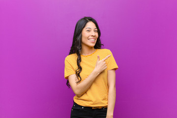 young pretty latin woman looking excited and surprised pointing to the side and upwards to copy...
