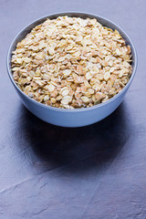 Dry oatmeal in bowl. Oat flakes on dark background. Cereals for making healthy breakfast. Vegetarian food. Copy space