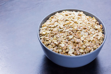Dry oatmeal in bowl. Oat flakes on dark background. Cereals for making healthy breakfast. Vegetarian food. Copy space