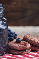 Fresh and tasty blueberry berries in a glass jar on a checkered napkin with sweet macaroons