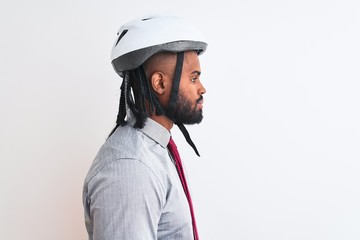 African american businessman with braids wearing bike helmet over isolated white background looking to side, relax profile pose with natural face with confident smile.