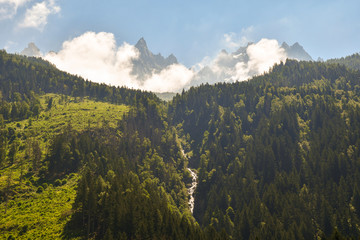 Mountain landscape with a waterfall among forest and the Aiguilles de Chamonix, a group of rocky...