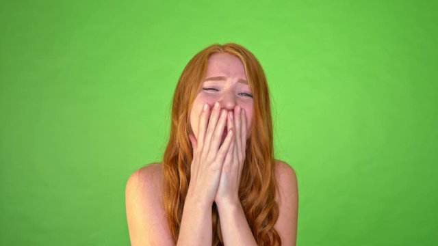 Happy young redheaded girl laughing and keeping hands at her face
