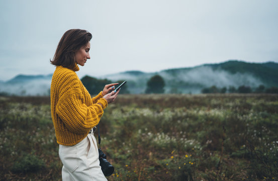 photographer girl hold in hands mobile phone typing message on smartphone on background autumn foggy mountain, mockup concept