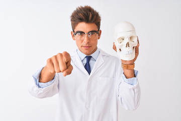 Young handsome doctor man wearing glasses holding skull over isolated white background pointing with finger to the camera and to you, hand sign, positive and confident gesture from the front