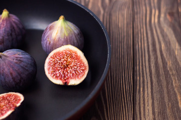 Fresh ripe figs in a dark pan on a wooden table. Healthy Mediterranean figs, selective focus