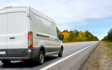 Fototapeta na wymiar White van drives a country road on autumn landscape background
