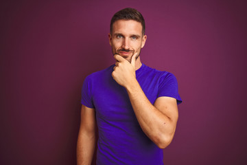 Young man wearing casual purple t-shirt over lilac isolated background looking confident at the camera with smile with crossed arms and hand raised on chin. Thinking positive.