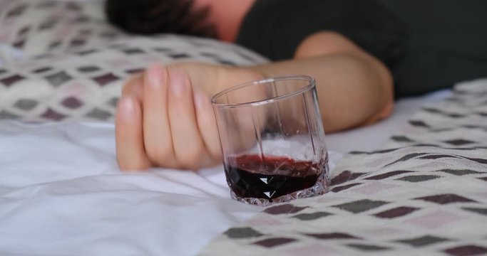 Man hand putting down glass of alcohol on bed sheets and twitching like in a seizure.