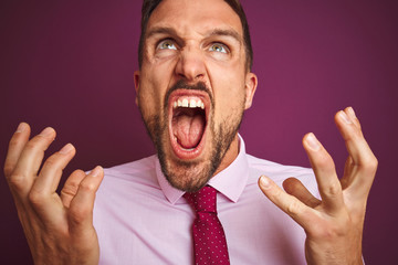 Close up of business man wearing elegant shirt and tie over purple isolated background crazy and mad shouting and yelling with aggressive expression and arms raised. Frustration concept.