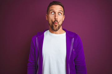 Obraz premium Young fitness man wearing casual sports sweatshirt over purple isolated background making fish face with lips, crazy and comical gesture. Funny expression.
