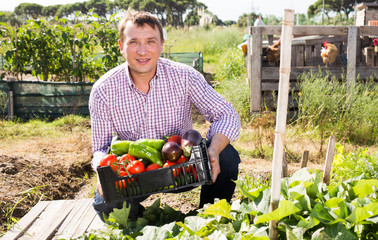 Man holding basket with harvest of vegetables, near chicken house
