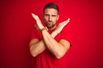 Young handsome man wearing casual t-shirt over red isolated background Rejection expression crossing arms doing negative sign, angry face