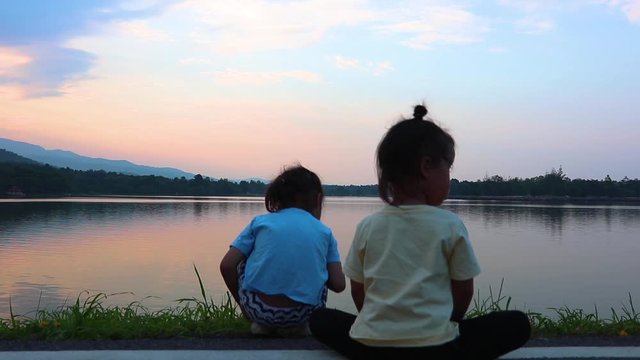 Happy children boy and girl brother and sister play together stand back and looking lake on sunset.