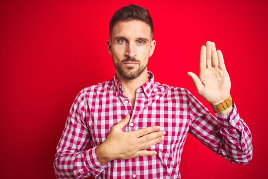 Young handsome man over red isolated background Swearing with hand on chest and open palm, making a loyalty promise oath