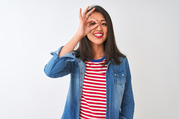 Obraz na płótnie Canvas Young chinese woman wearing striped t-shirt and denim shirt over isolated white background doing ok gesture with hand smiling, eye looking through fingers with happy face.