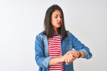 Young chinese woman wearing striped t-shirt and denim shirt over isolated white background Checking the time on wrist watch, relaxed and confident