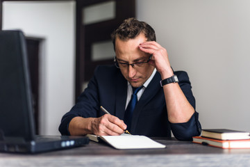 Attractive and confident businessman using mobile laptop computer and taking notes while working at...