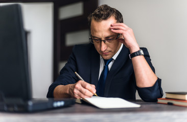 Obraz premium Businessman using mobile laptop computer and taking notes while working at the wooden table office.