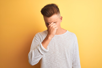 Young handsome man wearing white casual t-shirt standing over isolated yellow background tired rubbing nose and eyes feeling fatigue and headache. Stress and frustration concept.