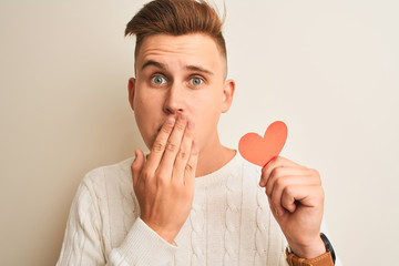 Young handsome romantic man holding paper hearts standing over isolated white background cover mouth with hand shocked with shame for mistake, expression of fear, scared in silence, secret concept
