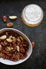 flat lay photo a glass of beer with white bowl of nuts on dark gray background