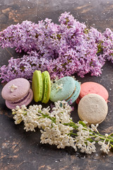 macaroon cakes lie on a wooden background, in composition with white and dark lilacs