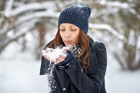 Beautiful girl blowing snow off her hands. Outdoor winter portrait