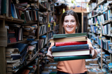 girl student holds a stack of books in the library, she searches for literature and offers to read,...