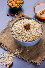 Dry oatmeal, nuts and honey. Oatmeal and almond nuts on dark background. Cereal and peanuts for making healthy breakfast. Oatmeal on burlap