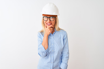 Middle age architect woman wearing glasses and helmet over isolated white background looking confident at the camera with smile with crossed arms and hand raised on chin. Thinking positive.