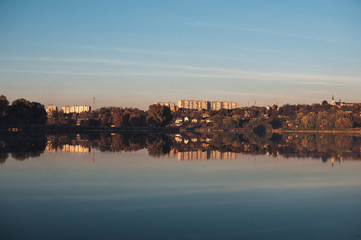Fototapeta premium Orange sunset against the background of the river in September in the harvest season. Reflection in the water from the trees. Beautiful autumn landscape. Autumn colors are reflected in calm waters.