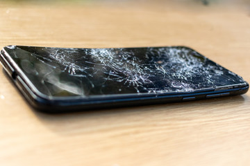 Broken screen cell phone on light  background. Old broken black smartphone on the table. Close up photos showing process of mobile phone repair. Smartphone and wooden hummer. 