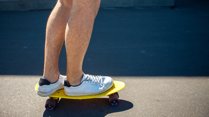 Legs in white sneakers are on a yellow skateboard with purple wheels. The correct setting of the legs on a skateboard.