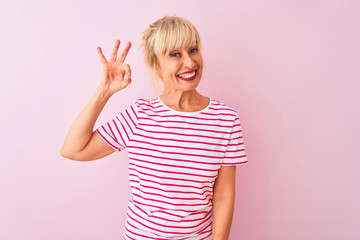 Middle age woman wearing striped t-shirt standing over isolated pink background smiling positive doing ok sign with hand and fingers. Successful expression.